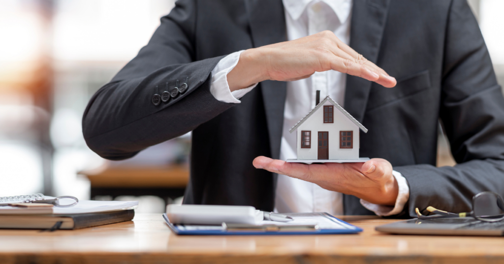 A man sitting at a desk in an office, holding a house model. 