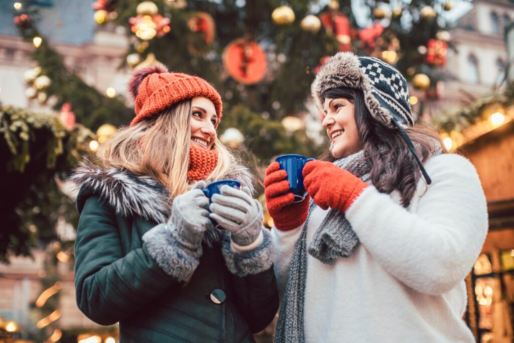 Best friends enjoying mulled wine on Christmas market looking at camera