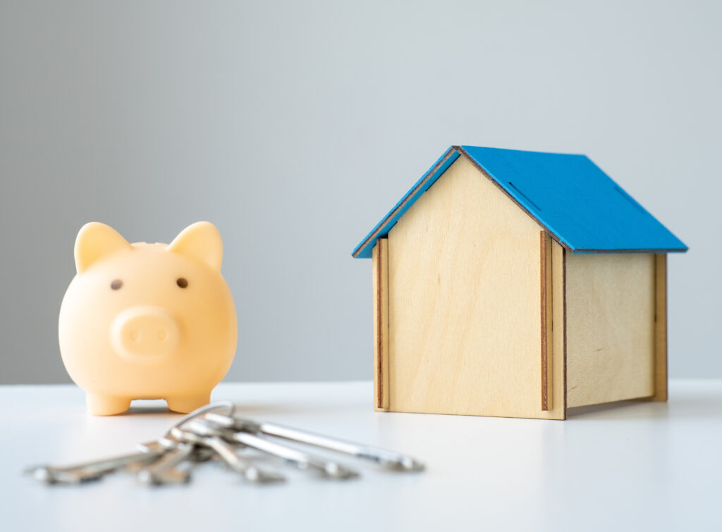 Piggy bank with keys and house model on the table. Savings for buy own home concept. Mortgage, home loan, investments in real estate