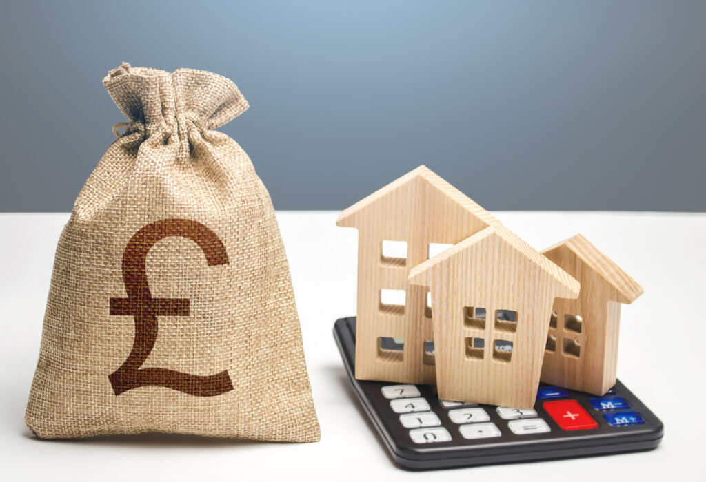Houses on a calculator and british pound sterling money bag. Buying and selling. Real estate valuation. Building maintenance. Mortgage loan. Utilities and services expenses. Taxes, budget.