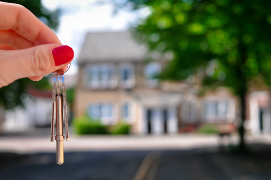 Woman's hand with metal keys on blurred background with house.