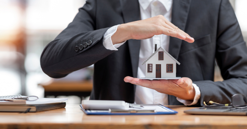A man sitting at a desk in an office, holding a house model.