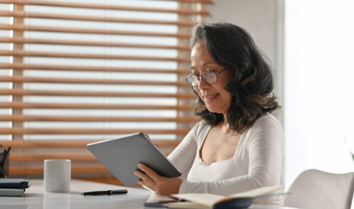 Woman reviewing property information on a tablet at home desk with notebook and coffee.