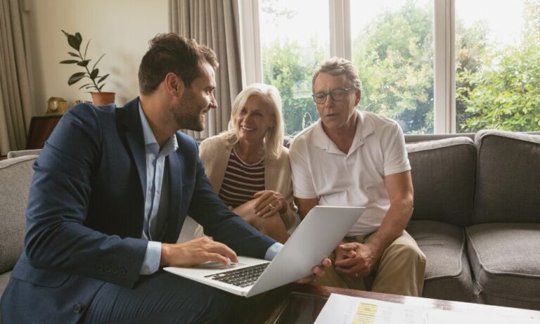 Estate agent discussing property options on a laptop with a mature couple in a living room