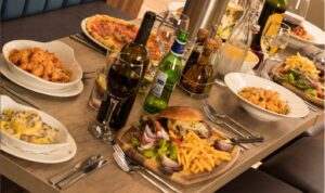 Table filled with burgers, pasta, pizza, fries, and drinks in a lively restaurant setting in Carlton Nottingham