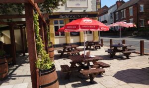 Outdoor seating area at The Old Volunteer pub in Carlton Nottingham with wooden benches and red umbrellas on a sunny day