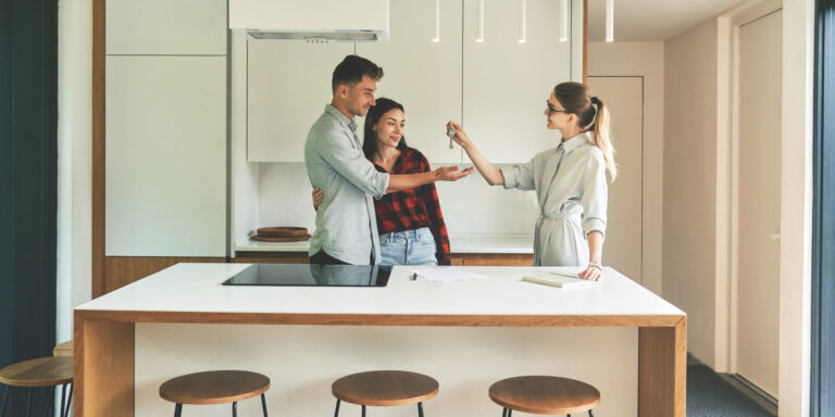 Estate agent handing keys to a couple in a modern kitchen, representing house valuations and buyer demand in Tamworth.