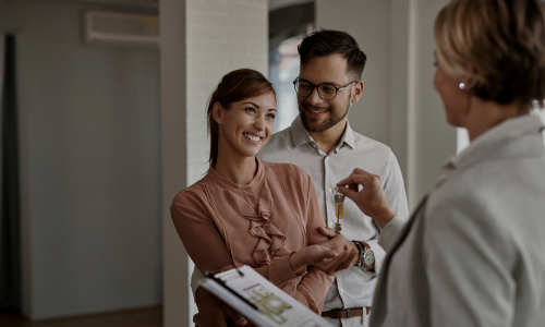 A happy couple receives the keys to their new home from an estate agent, illustrating a successful property sale and the strong buyer demand discussed in the Guiseley property market 2026 article.