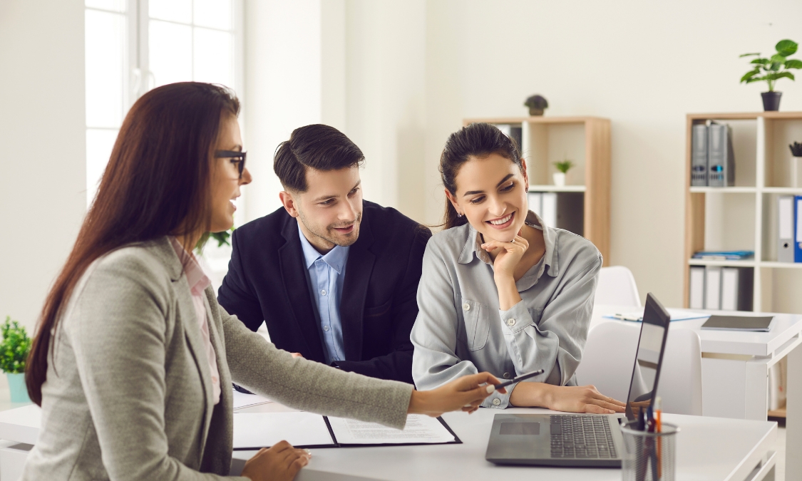 Estate agent discussing property details with a couple using a laptop during a home-selling consultation, illustrating expert advice for homeowners preparing to sell in Walsall's 2026 property market.
