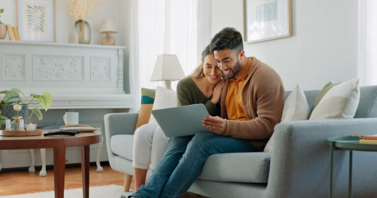 Couple sitting together on a sofa using a tablet while researching homes, reflecting buyers and renters exploring life in Guiseley LS20.