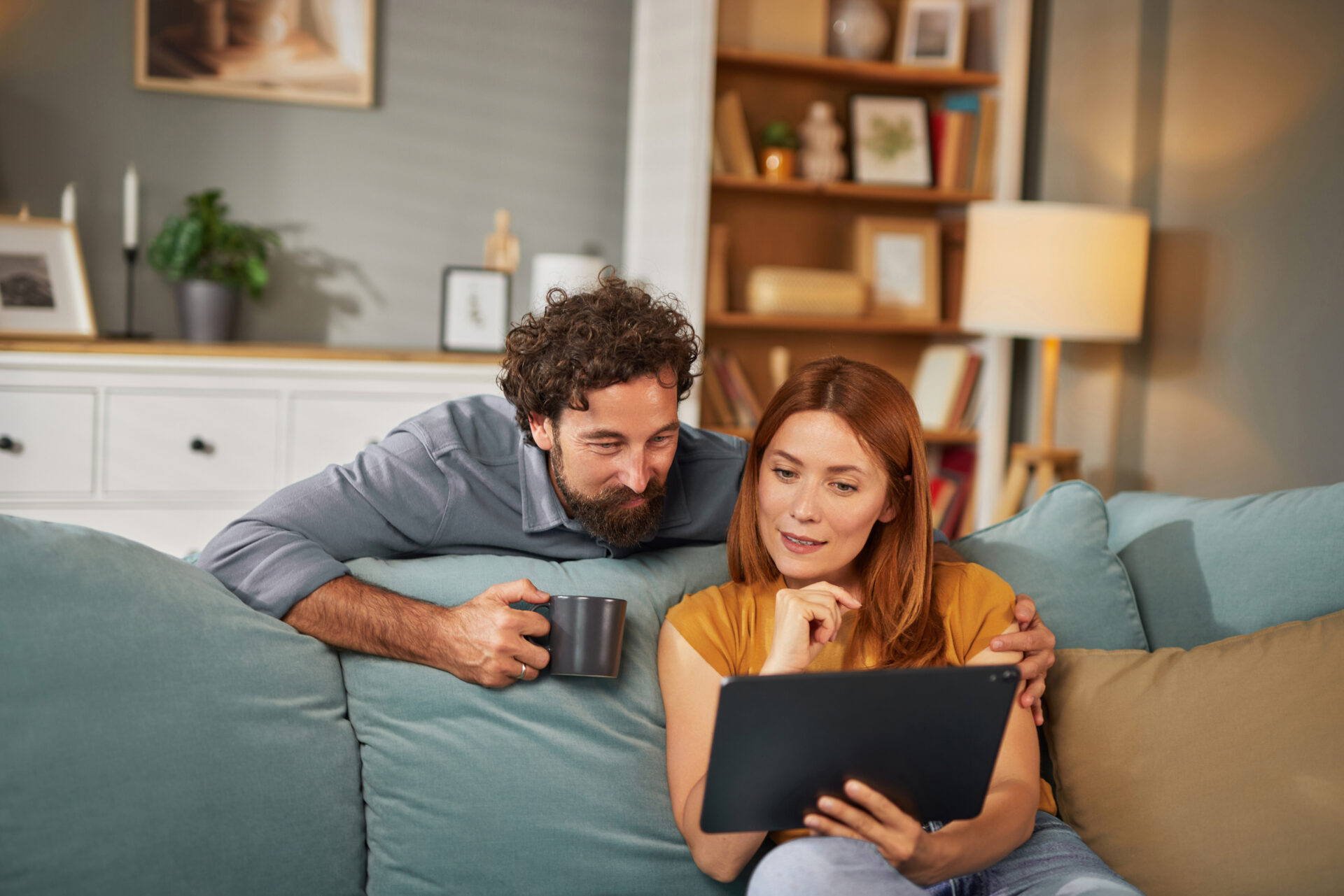 Couple relaxing on a sofa while using a tablet to research homes, representing buyers and renters exploring life in Morley LS27.