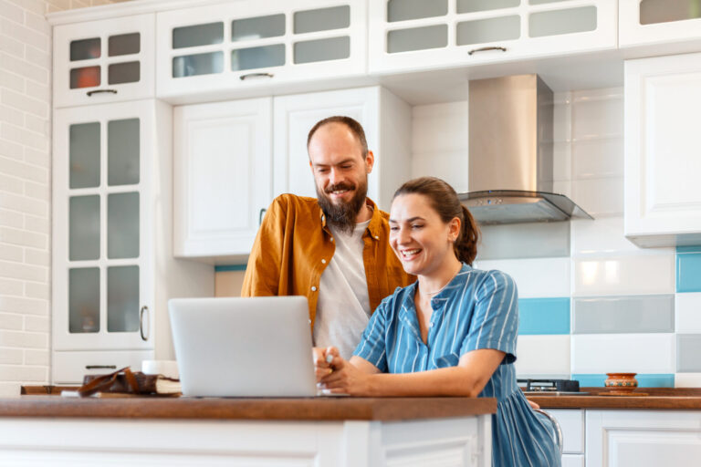 Couple using a laptop at home while researching the Stafford property market and considering selling their property.