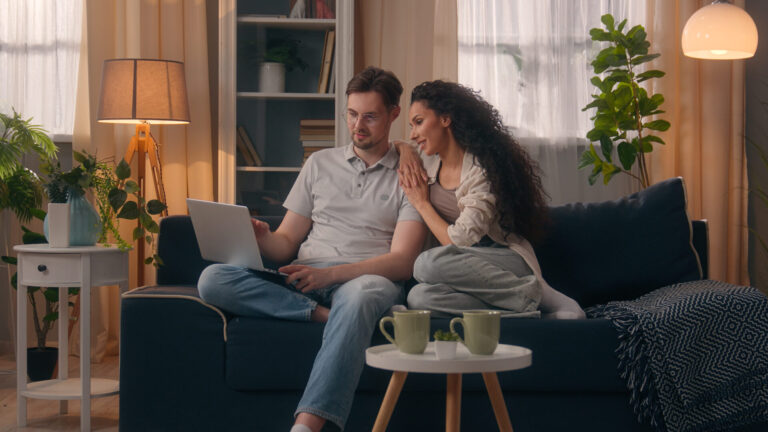 Couple using a laptop together while relaxing in their rented home